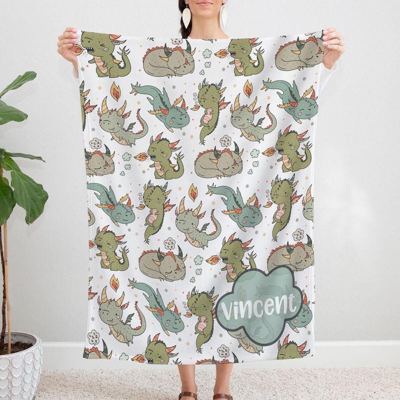 A person is holding up a white towel with a repeating pattern of green and orange cartoon-style dragons.