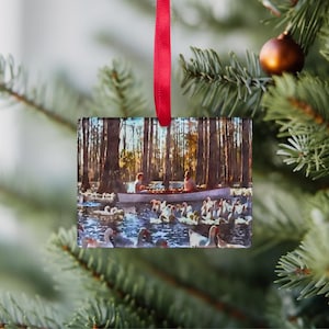 May include: A glass Christmas ornament featuring a vintage photograph of two people in a canoe surrounded by a flock of ducks in a forest setting.