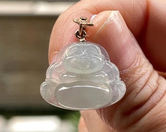 May include: A translucent, pale green jade pendant carved in the shape of a smiling Buddha figure. The pendant features a smooth, polished surface and is attached to a small, metallic gold-toned bail at the top for hanging on a chain.