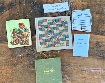 May include: A vintage Snakes and Ladders board game with a green box, a colorful game board, and score cards. The game board features a picture of a man playing a drum. The game is titled "Good Old Snakes & Ladders".