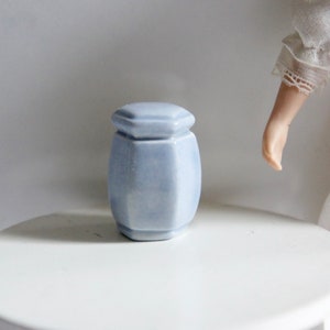 Könnte beinhalten: Eine kleine, hellblaue Keramikdose mit sechseckiger Form und Deckel. Die Dose steht auf einem weißen Tisch.