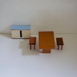 May include: A miniature dollhouse furniture set with a white cabinet with a light blue top, a brown table, and two brown chairs.