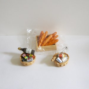 May include: A miniature wooden crate filled with miniature baguettes, a miniature wicker basket filled with miniature canned goods, and a miniature wine bottle. The items are arranged on a white surface.
