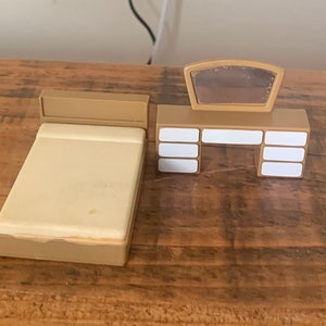 May include: A miniature dollhouse furniture set with a brown bed and a vanity with a mirror and drawers. The vanity has white drawer fronts.