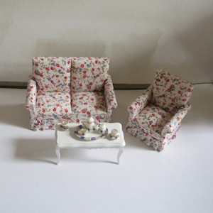 May include: A floral patterned dollhouse sofa and armchair set with a white coffee table and tea set.
