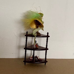 May include: A three-tiered wooden shelf with a green and yellow feathered hat on the top shelf and two pairs of shoes on the bottom shelf.