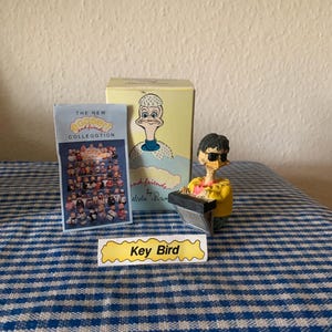 May include: A yellow figurine of a bird wearing sunglasses and playing a keyboard. The figurine is part of a collection called "The New Eggbert and Friends Collection by Alden Brown".