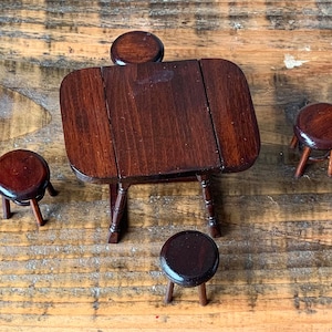 Puede incluir: Un juego de mesa y sillas de madera en miniatura. La mesa y las sillas son de color marrón oscuro y tienen un acabado rústico. El juego está dispuesto sobre una superficie de madera.
