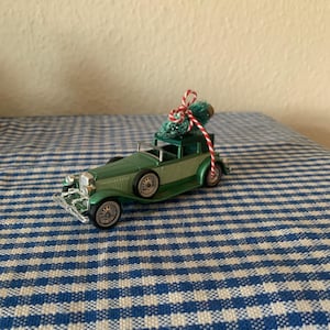 May include: A green vintage car toy with a small green Christmas tree tied to the roof with red and white twine.