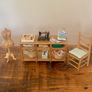 May include: A miniature wooden sewing station with a sewing machine, fabric scraps, and a small chair. The station has two shelves with baskets and a wooden mannequin.