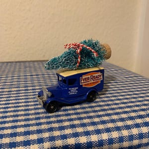 Puede incluir: Un camión de juguete azul con techo blanco y las palabras "Ever Ready Made in Britain" en el lateral. El camión lleva un pequeño árbol de Navidad azul y blanco con una cinta roja y blanca.