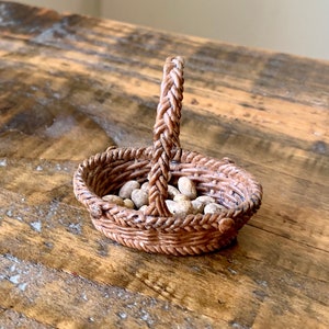May include: A small brown wicker basket with a woven handle filled with white pebbles.