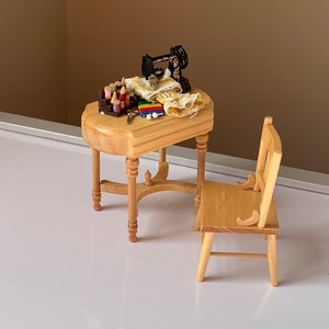 May include: A miniature wooden table and chair set with a sewing machine and fabric scraps on the table.