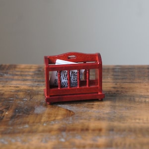 May include: A red wooden magazine rack with a white paper magazine inside. The rack is sitting on a wooden surface.