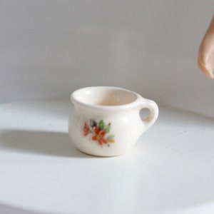 Pode incluir: Um pequeno penico de cerâmica branca com um desenho floral em tons de laranja e verde.