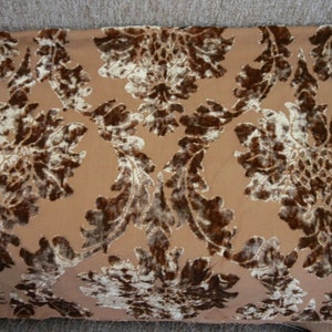 May include: A close-up of a brown fabric with a white and brown floral pattern. The fabric has a textured, velvety surface.