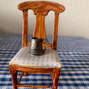 May include: Miniature wooden chair with a light blue and white checkered cushion. A small metal tankard with the text "Whitbread Tankard" sits on the chair. The chair has a dark brown finish.