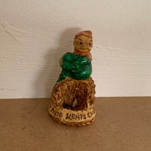 Op de afbeelding: Een keramiek beeldje van een kabouter met een groen shirt en een rode muts. De kabouter zit in een nestvormige basis met de tekst "Petite Kents Cave" erop.