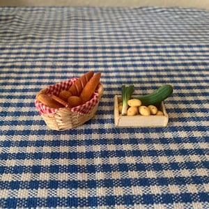 Può includere: Un cestino di vimini in miniatura con una fodera a quadri rosso e bianco riempito di pagnotte di pane in miniatura, e una cassetta di legno in miniatura piena di patate in miniatura e cipolle verdi.