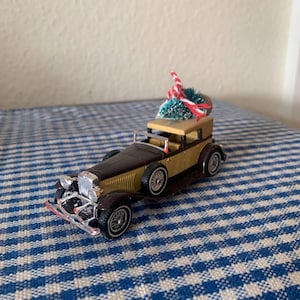 May include: A brown and gold toy car with a small green Christmas tree on top. The car is on a blue and white checkered tablecloth.