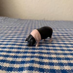 May include: A black and pink plastic pig figurine. The pig is standing on a blue and white checkered surface.