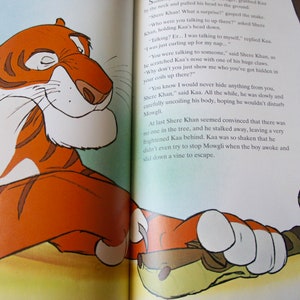 Puede incluir: Un primer plano de un tigre y una serpiente del libro "El libro de la selva". El tigre es naranja y negro con rayas blancas. La serpiente es verde y marr&oacute;n con un patr&oacute;n de escamas. El texto de la imagen dice: "&iquest;Con qui&eacute;n estabas hablando ah&iacute; arriba?" pregunt&oacute; Shere Khan. "Hablando conmigo mismo." respondi&oacute; Kaa. "Sabes que nunca te esconder&iacute;a nada, Shere Khan." dijo Kaa. Todo el tiempo, estaba desenrollando lentamente y con cuidado su cuerpo, con la esperanza de no molestar a Mowgli. Finalmente, Shere Khan pareci&oacute; convencido de que no hab&iacute;a nadie en el &aacute;rbol, y se fue, dejando a un Kaa muy asustado atr&aacute;s. Kaa estaba tan conmocionado que ni siquiera intent&oacute; detener a Mowgli cuando el ni&ntilde;o despert&oacute; y se desliz&oacute; por una enredadera para escapar.