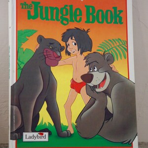 Puede incluir: Una portada de libro vintage de Disney con los personajes Mowgli, Bagheera y Baloo de El Libro de la Selva. La portada es naranja y verde con el t&iacute;tulo "El Libro de la Selva" en letras verdes. El libro est&aacute; publicado por Ladybird.