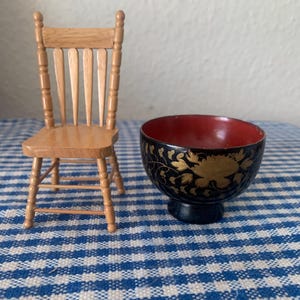 May include: A miniature wooden chair with a slatted back and a black and gold painted wooden bowl with floral designs.
