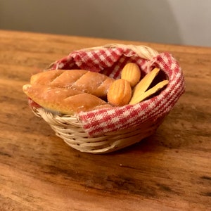 Op de afbeelding: Een kleine rieten mand bekleed met een rood-wit geruite doek gevuld met broodjes en broden.