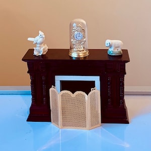 May include: A miniature wooden fireplace mantel with a white porcelain figurine of a bird, a glass dome clock, and a white porcelain figurine of a sheep. The fireplace has a gold metal fire screen.