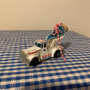 May include: A white toy truck with "SUPER BOSS" written on the side is carrying a small green Christmas tree tied with red and white string.