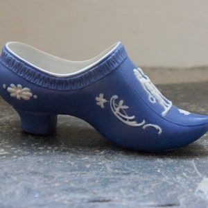 May include: A blue ceramic shoe with white floral and figure designs. The shoe has a high heel and a pointed toe.