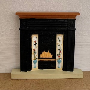 Peut inclure: Une cheminée miniature noire avec un manteau blanc et un foyer décoratif. La cheminée a un dessus en bois brun et une base blanche.