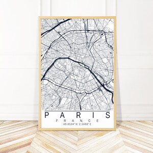 以下が含まれることがあります： フランスのパリ市の白黒地図で、都市名と座標が下に印刷されています。地図は明るい木製のフレームで額装されています。