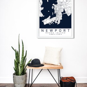 May include: A framed map of Newport, Rhode Island, with a white frame and a dark blue background. The map shows the city's streets and waterways. The text "NEWPORT RHODE ISLAND 41.4900&deg;N 71.3138&deg;W" is printed below the map.