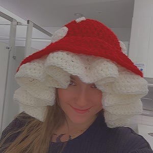 May include: A whimsical, handmade crochet mushroom hat. The hat features a vibrant red top with white polka dots and a ruffled, off-white brim. This unique accessory is perfect for costume parties or adding a touch of fantasy to any outfit.