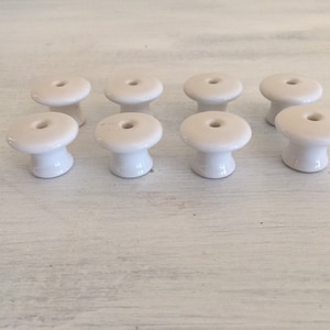 May include: Ten white ceramic knobs with a round top and a small hole in the center. The knobs have a slightly raised base.