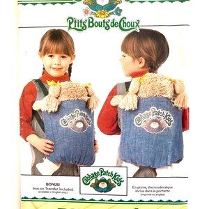 May include: A vintage Butterick sewing pattern featuring Cabbage Patch Kids. The pattern includes instructions for making a doll carrier. The cover shows a child wearing the carrier, with the Cabbage Patch Kids logo and the text "Ptits Bouts de Choux".