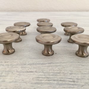 May include: Twelve silver cabinet knobs with a circular design and a raised center. The knobs have a smooth, polished finish.