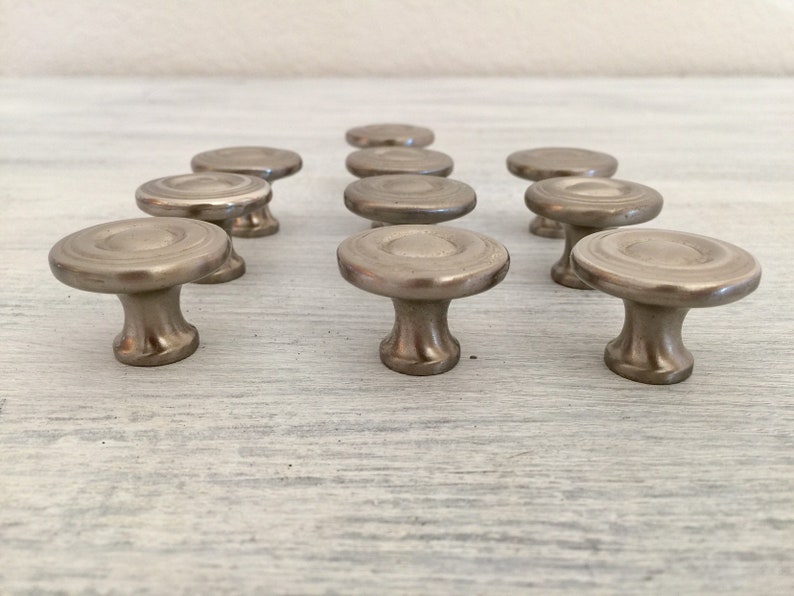 May include: Twelve silver cabinet knobs with a circular design and a raised center. The knobs have a smooth, polished finish.