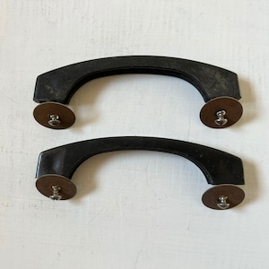 May include: Two black plastic handles with silver metal accents. The handles are curved and have a smooth surface.