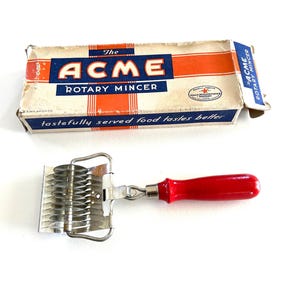 May include: Vintage Acme Rotary Mincer in its original box. The mincer has a red handle and a silver metal blade. The box is white with red and blue accents and the text "The Acme Rotary Mincer" printed on it.