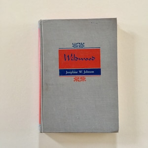 May include: A gray hardcover book with the title "Wildwood" in blue lettering on a red background. The author, Josephine W. Johnson, is printed in blue below the title.