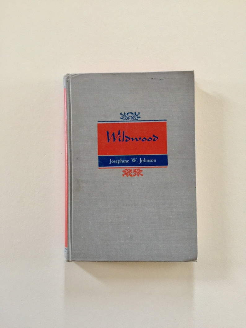 May include: A gray hardcover book with the title "Wildwood" in blue lettering on a red background. The author, Josephine W. Johnson, is printed in blue below the title.
