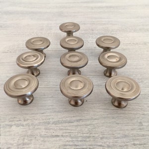 May include: Twelve silver cabinet knobs with a circular design and a raised center. The knobs have a satin finish and are arranged in a triangular pattern.