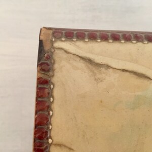 May include: Close-up of the top edge of a vintage photo album with a red and white border. The album is made of leather and has a worn, aged look.