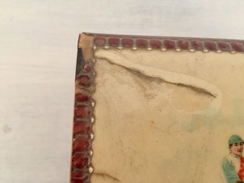 May include: Close-up of the top edge of a vintage photo album with a red and white border. The album is made of leather and has a worn, aged look.