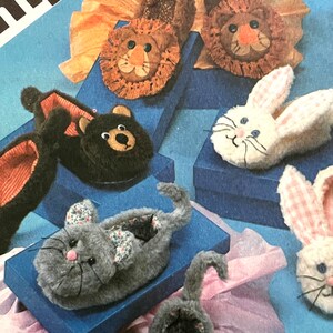 May include: A set of five animal-shaped slippers. The slippers are made of soft, plush fabric and feature embroidered faces. The animals include a lion, a bear, a bunny, and two cats.