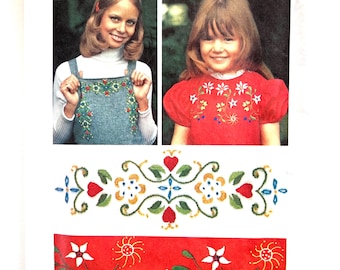 May include: Simplicity embroidery design pattern. The pattern features two children's clothing designs with floral embroidery. The pattern includes a red border with white flowers and a green and blue border with hearts and flowers.