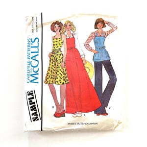 May include: A vintage McCall's sewing pattern envelope featuring three women wearing different styles of aprons. The pattern is for a misses' butcher apron. The envelope is labeled "Sample" and "Carefree Patterns".